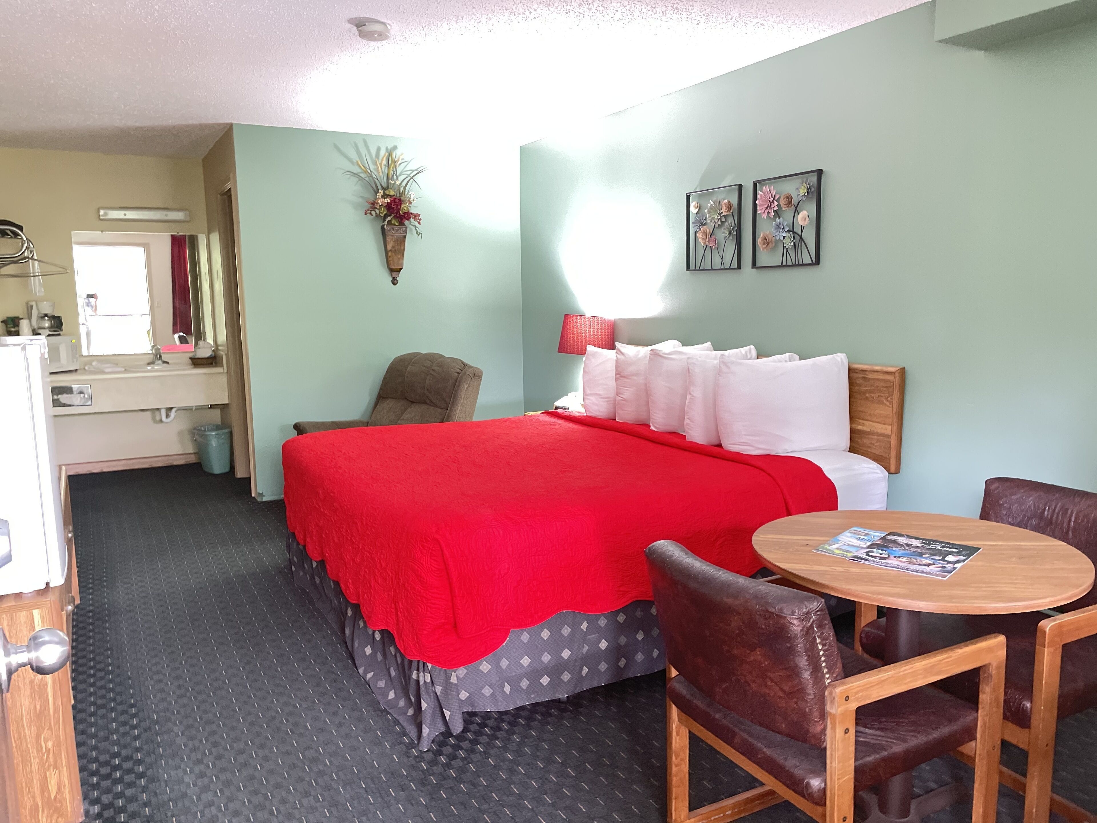 Une chambre d’hôtel avec un lit, une chaise, une petite table, un lavabo et un miroir.