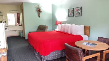 A hotel room with a bed, a chair, a small table, a sink, and a mirror.