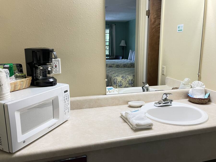 A hotel bathroom with a white sink, a mirror, a coffee maker, and a microwave.