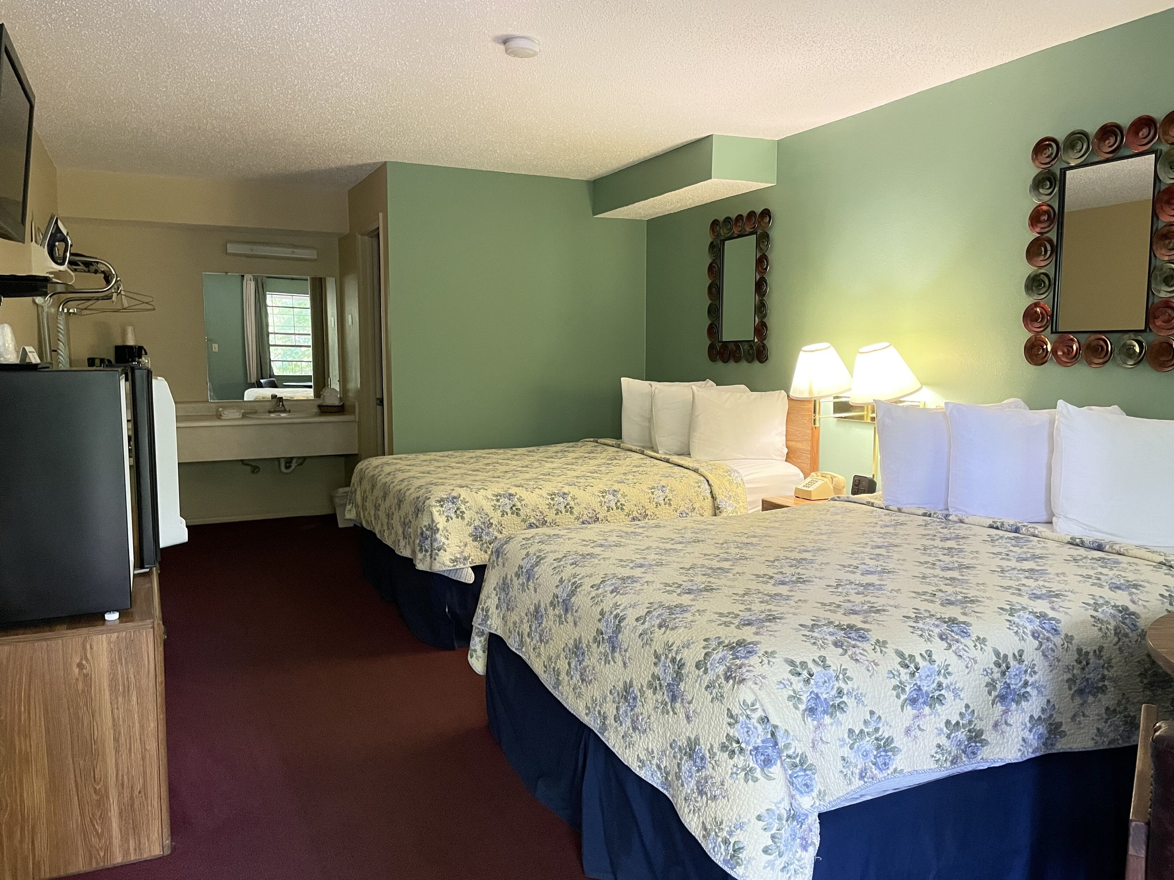 Une chambre d’hôtel avec deux lits, une télévision, un miroir et une fenêtre avec des stores.