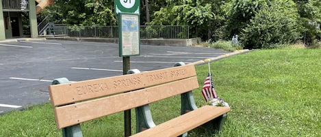 A trolley stop sign with a bench labeled "Eureka Springs' Transit System" and an American flag.