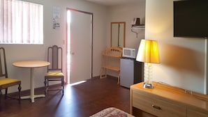 A small, well-lit room with a wooden chair, a small table, a microwave, a lamp, and a TV mounted on the wall. - Alpine Motel (Wisconsin Dells)