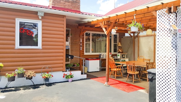 A wooden house with a red roof, a sign indicating it's open, and a table with chairs outside. - Alpine Motel (Wisconsin Dells)