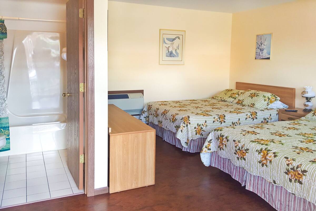 Una habitación de hotel con dos camas, un escritorio de madera y un baño con bañera y retrete.