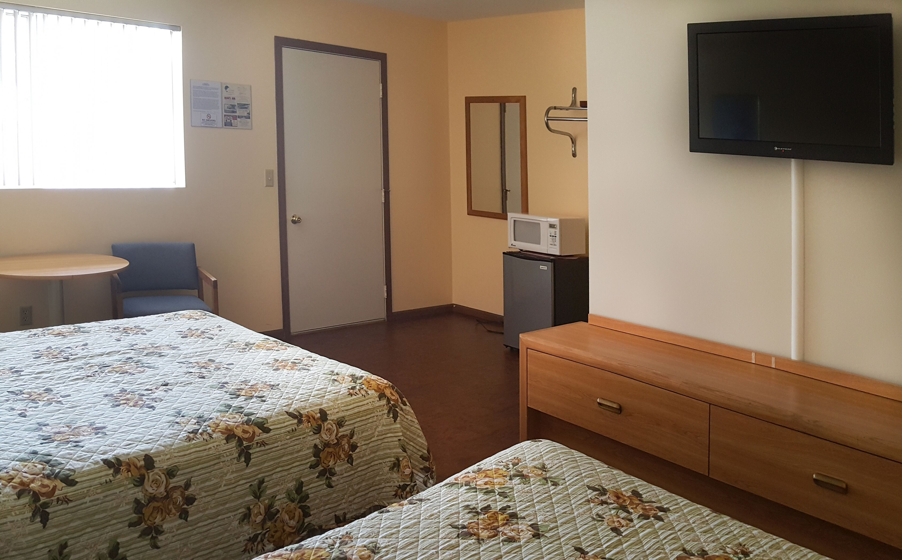 Hotellihuone, jossa on kaksi sänkyä, pieni pöytä, tuoli, televisio, mikroaaltouuni ja lipasto.