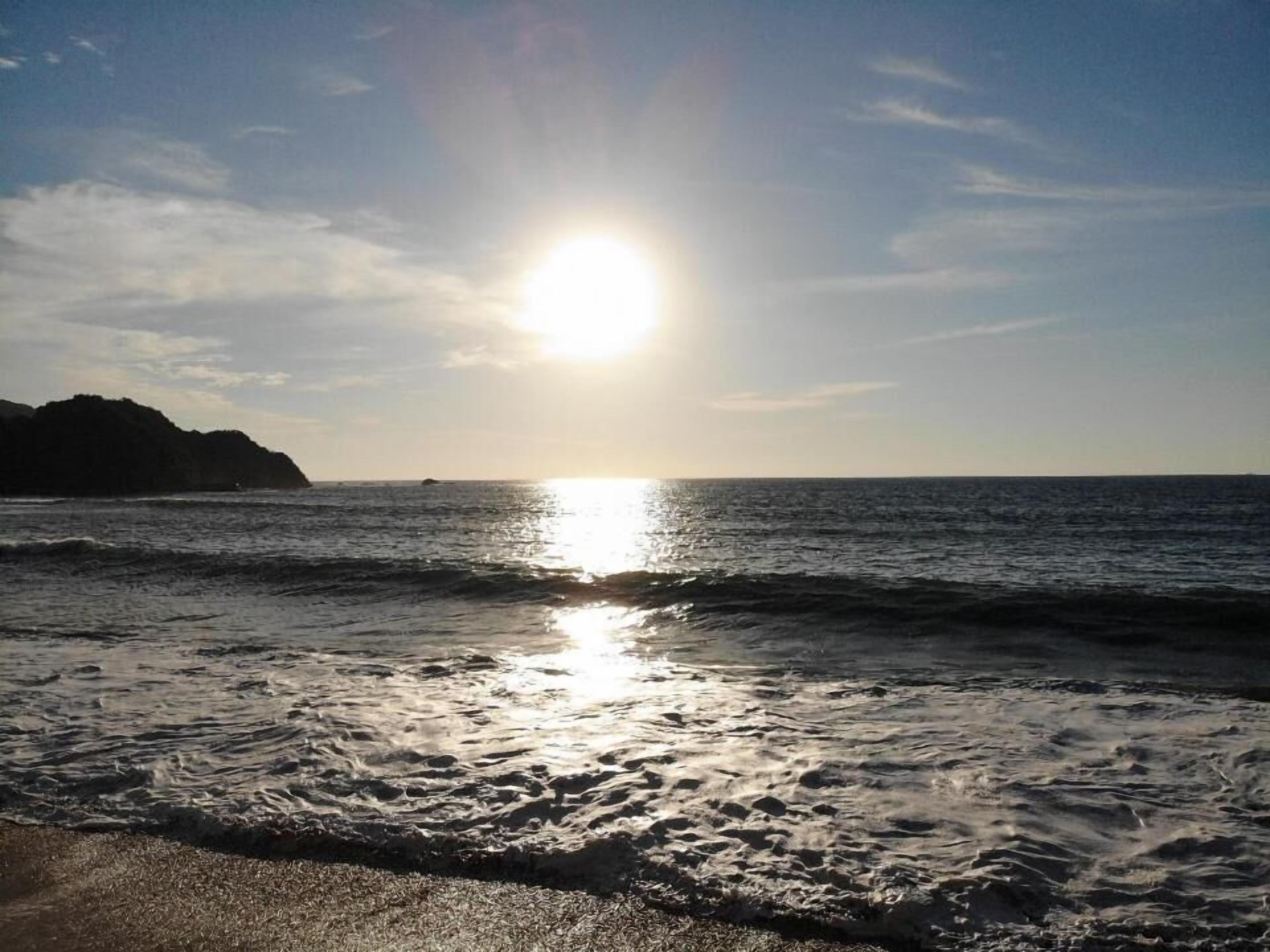 Een strand met golven en een zon die in het water glinstert.