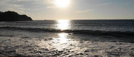 Una playa con olas y el sol reflejado en el agua.
