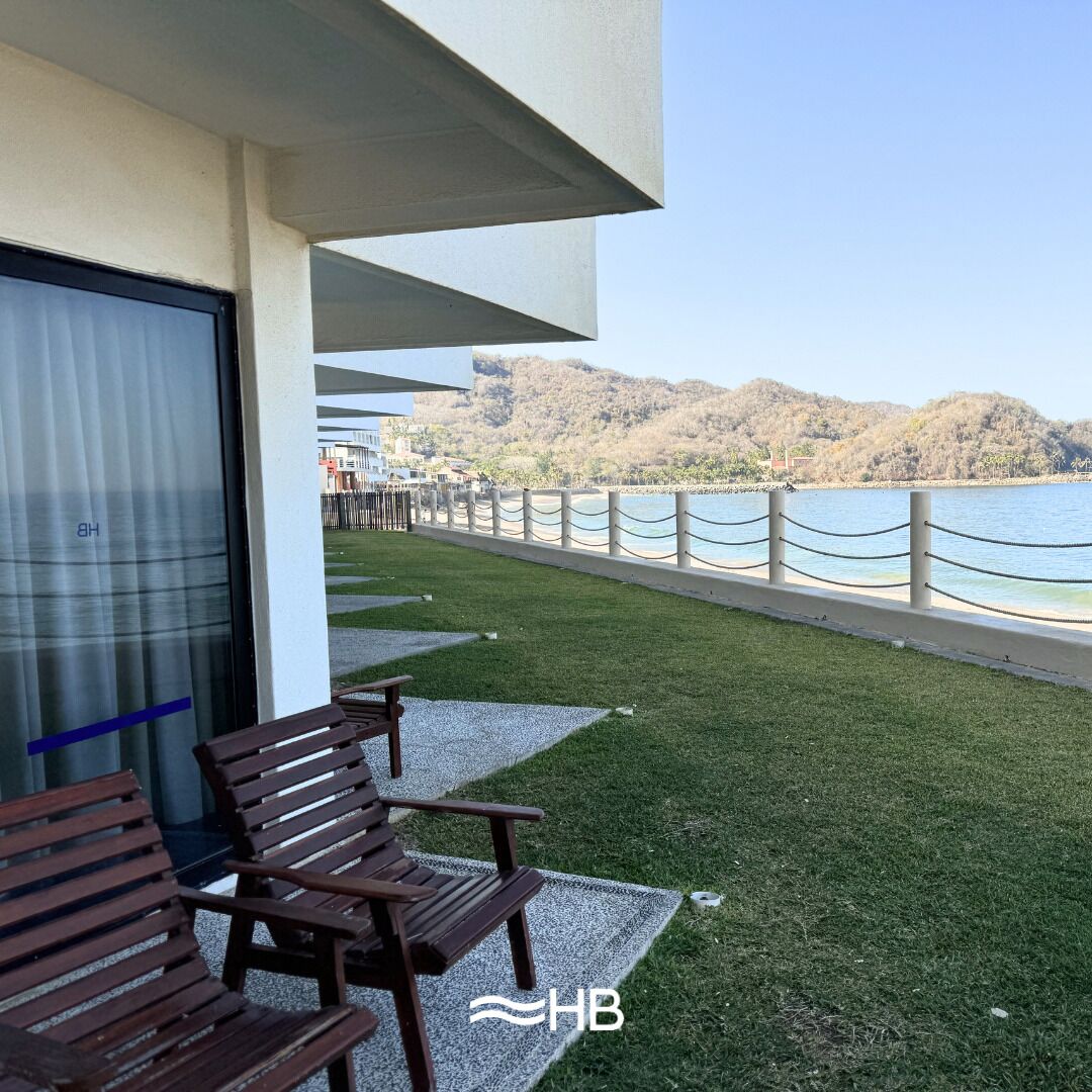 A balcony with wooden benches, a view of the sea, and a mountainous landscape in the background.