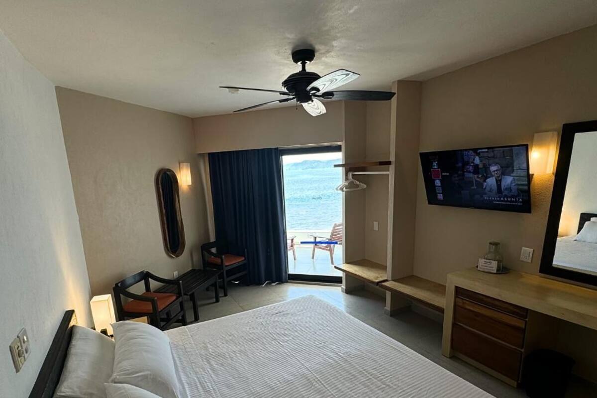 Habitación de hotel con cama, escritorio, silla, televisor y vista al océano.