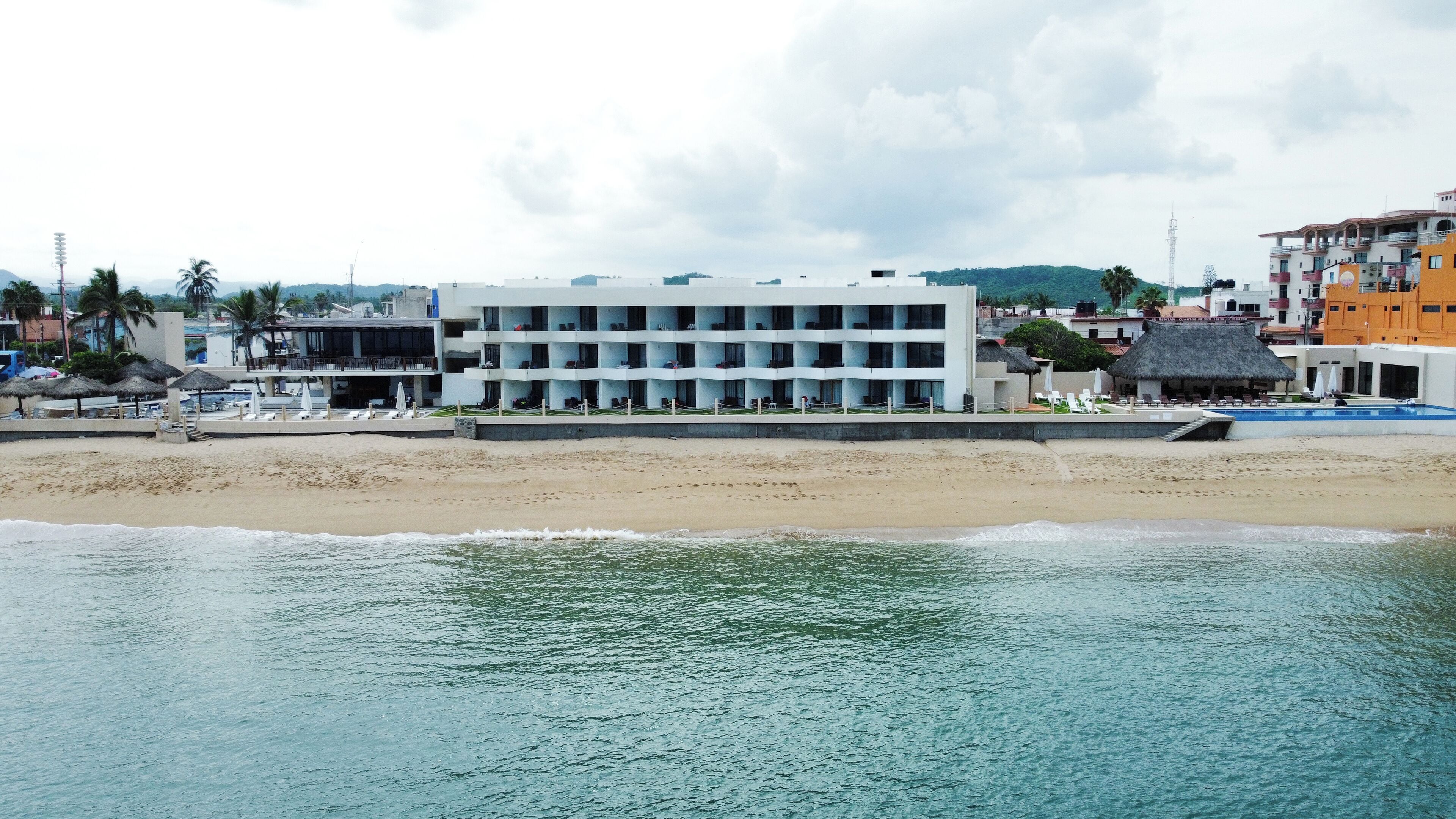 A beachfront hotel with multiple balconies, a pool area, and a beach view.