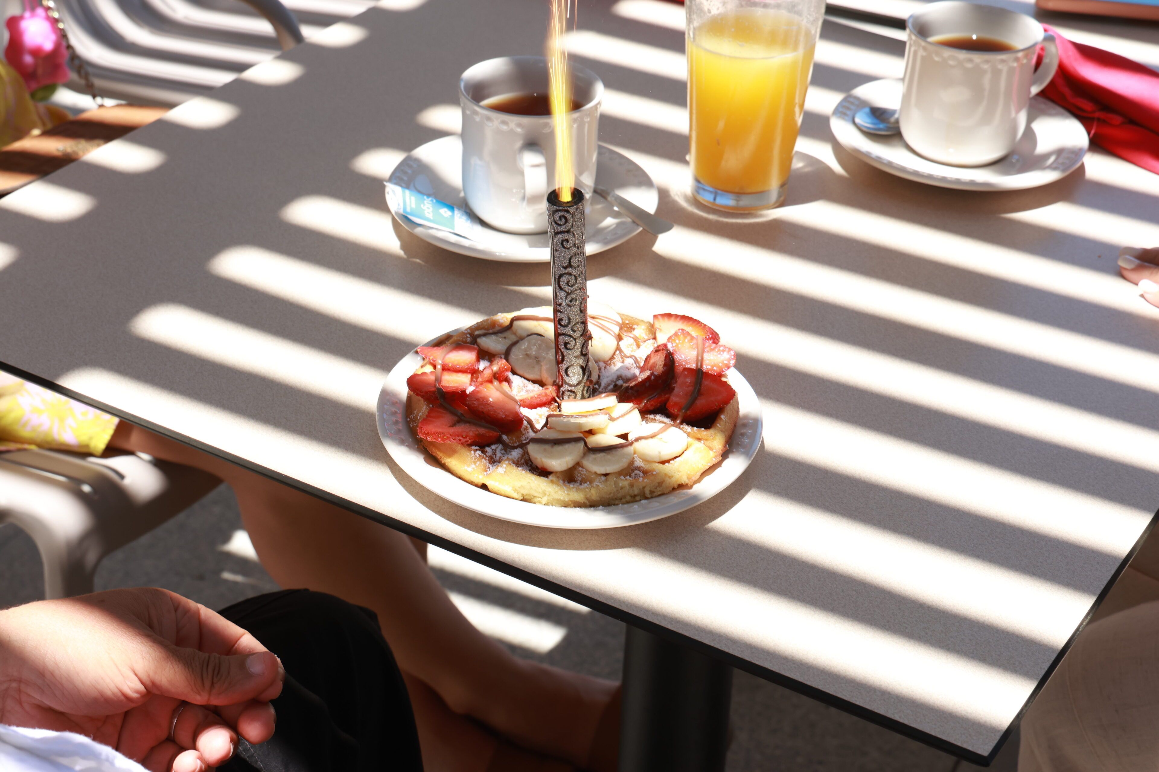 Un desayuno con un plato de comida, una taza de café y un vaso de zumo de naranja sobre una mesa con estampado a rayas.