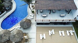 Vista aérea de un resort con piscina, mobiliario exterior y una zona cubierta.