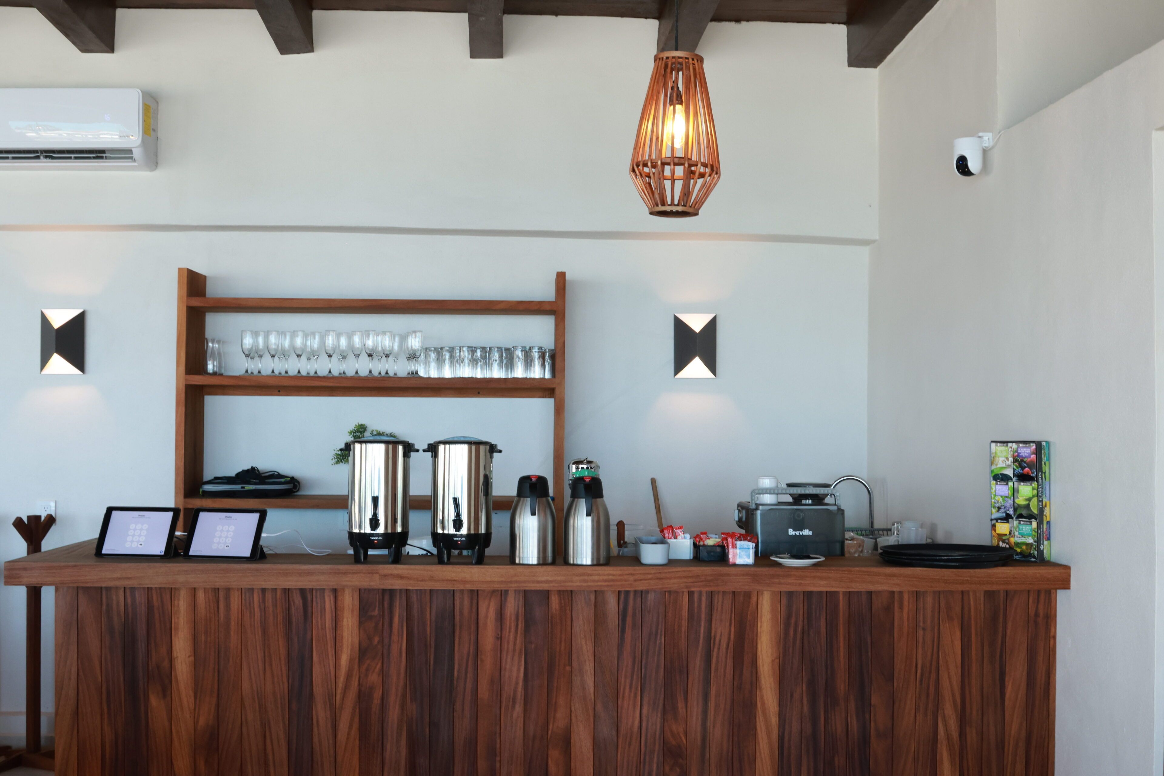 Una encimera de madera con cafeteras, un aparato Breville y una estantería con vasos.