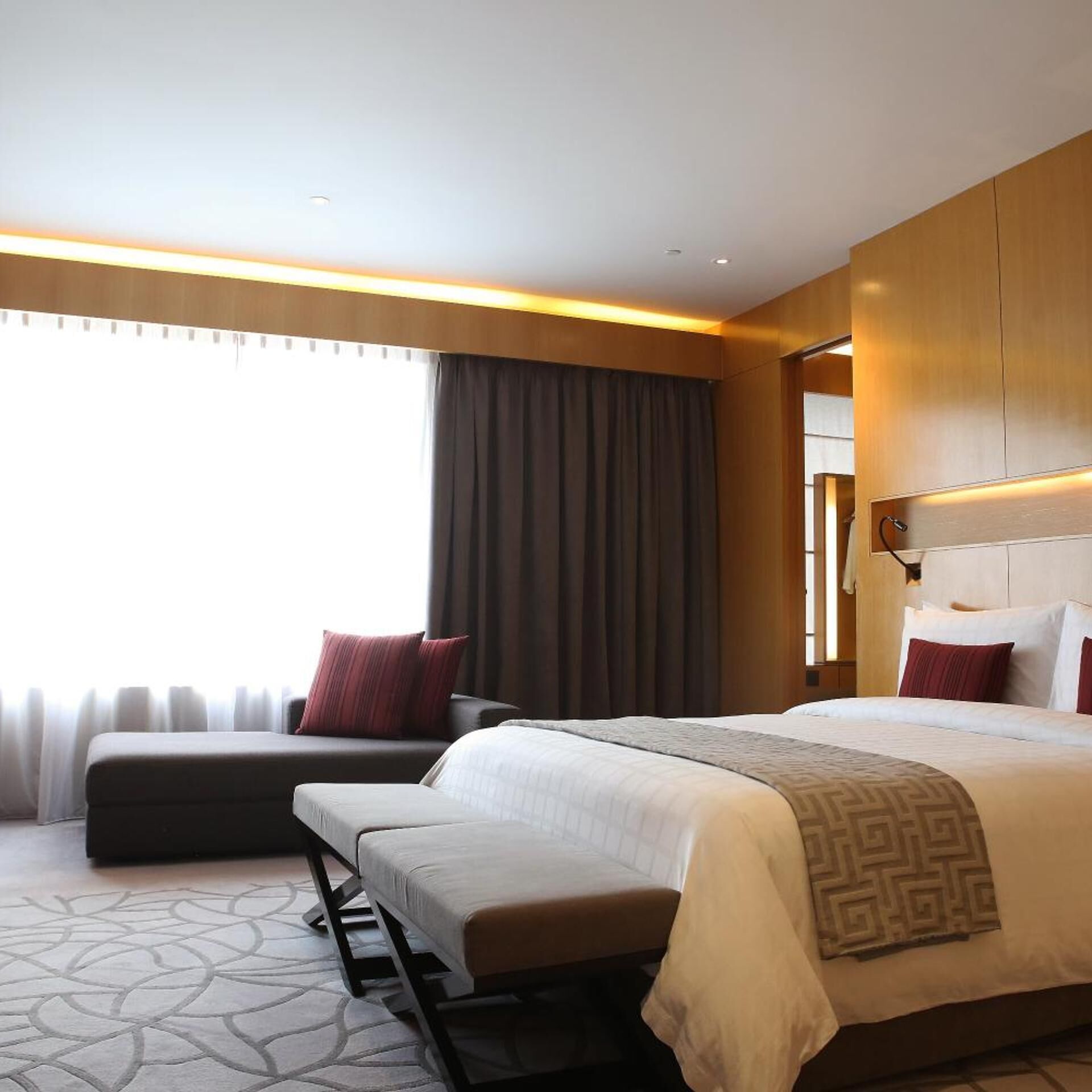 A hotel room with a large bed, a sofa, a small table, and a window with curtains.