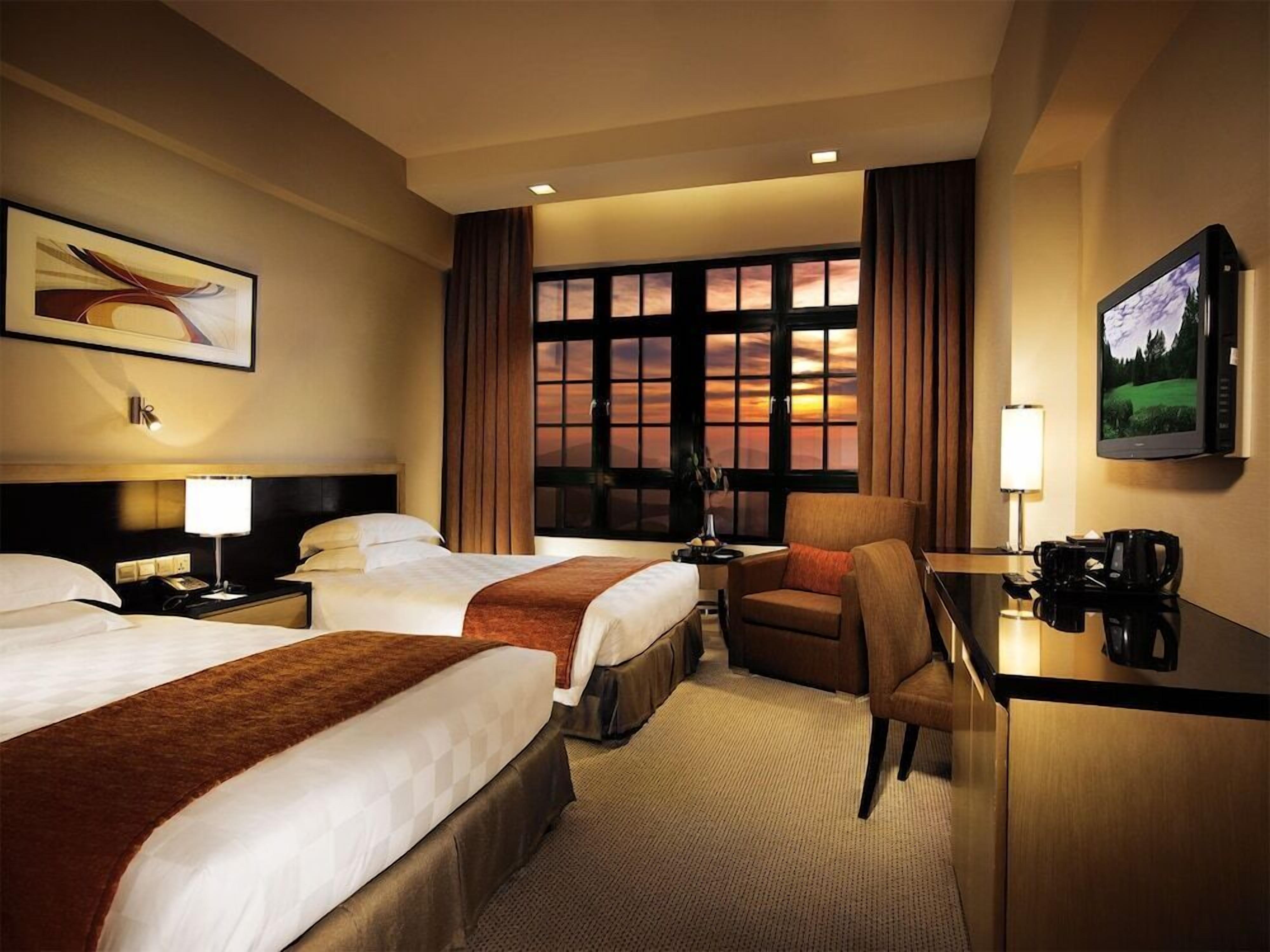 A hotel room with two beds, a desk, a chair, a TV, and a large window with curtains.