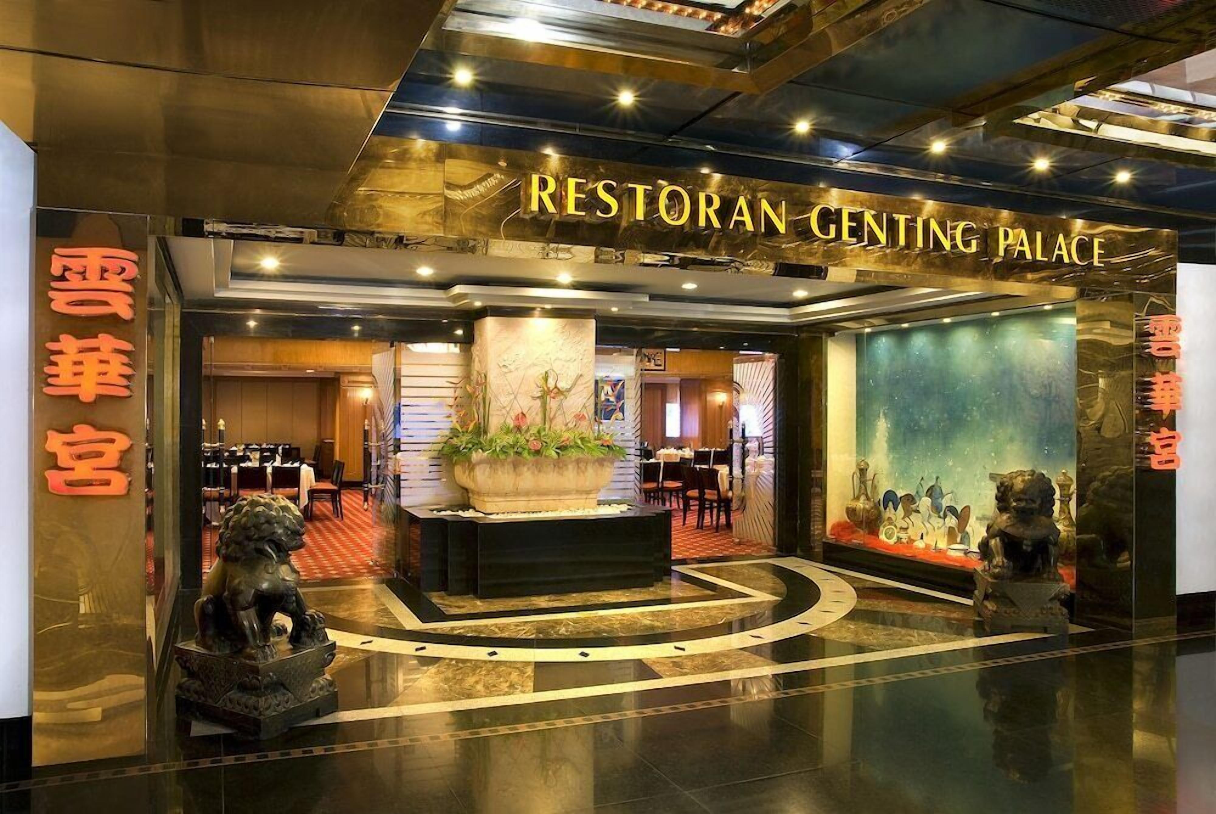 A hotel entrance with a sign reading 'Restoran Genting Palace,' a large flower arrangement, and a statue of a lion.