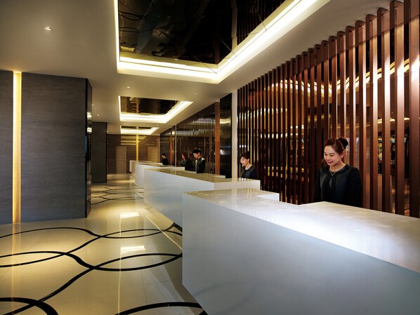 Un área de recepción moderna con un mostrador elegante, piso con diseño y paneles de madera verticales a la derecha.