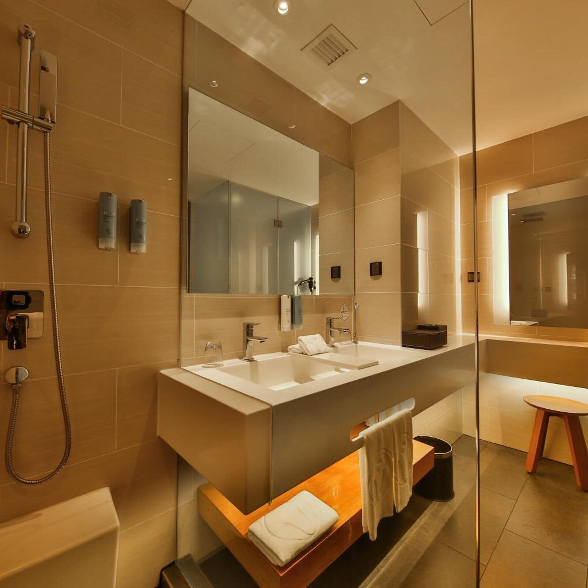 A modern bathroom with a large mirror, two sinks, a shower, and a glass-enclosed vanity.