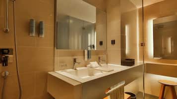 A modern bathroom with a large mirror, two sinks, a shower, and a glass-enclosed vanity.