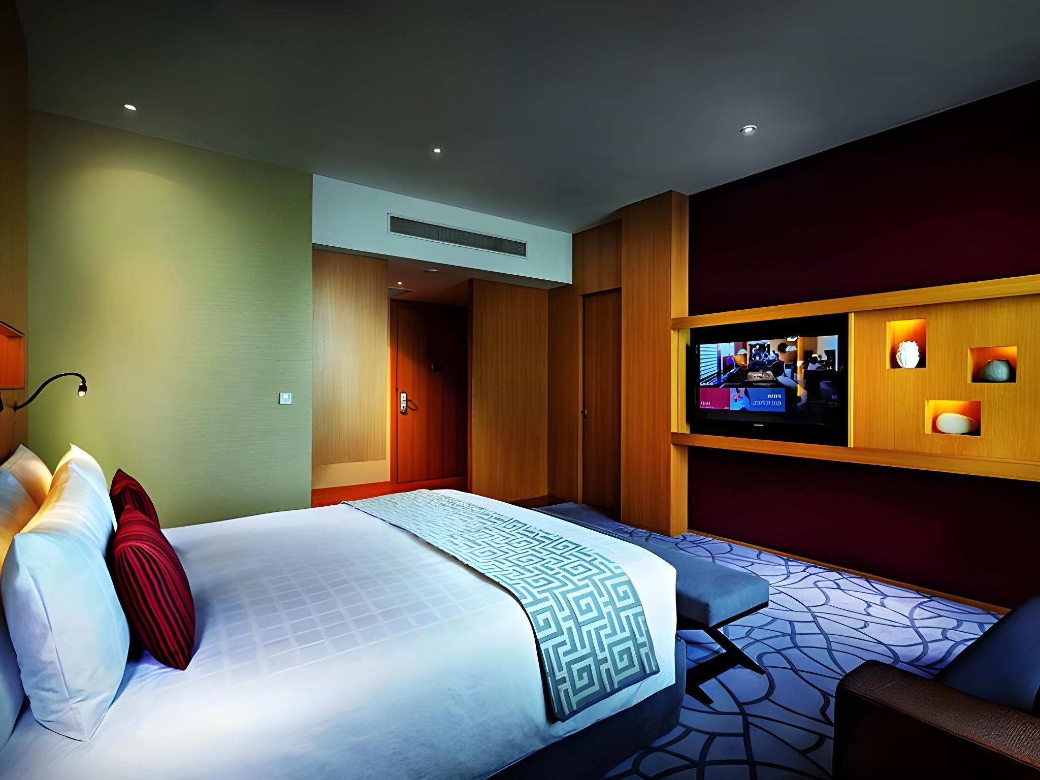 A hotel room with a bed, a TV mounted on the wall, a desk, and a chair.