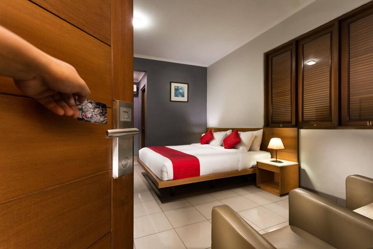 A hotel room with a wooden bed, a nightstand with a lamp, a seating area, and a framed picture on the wall.