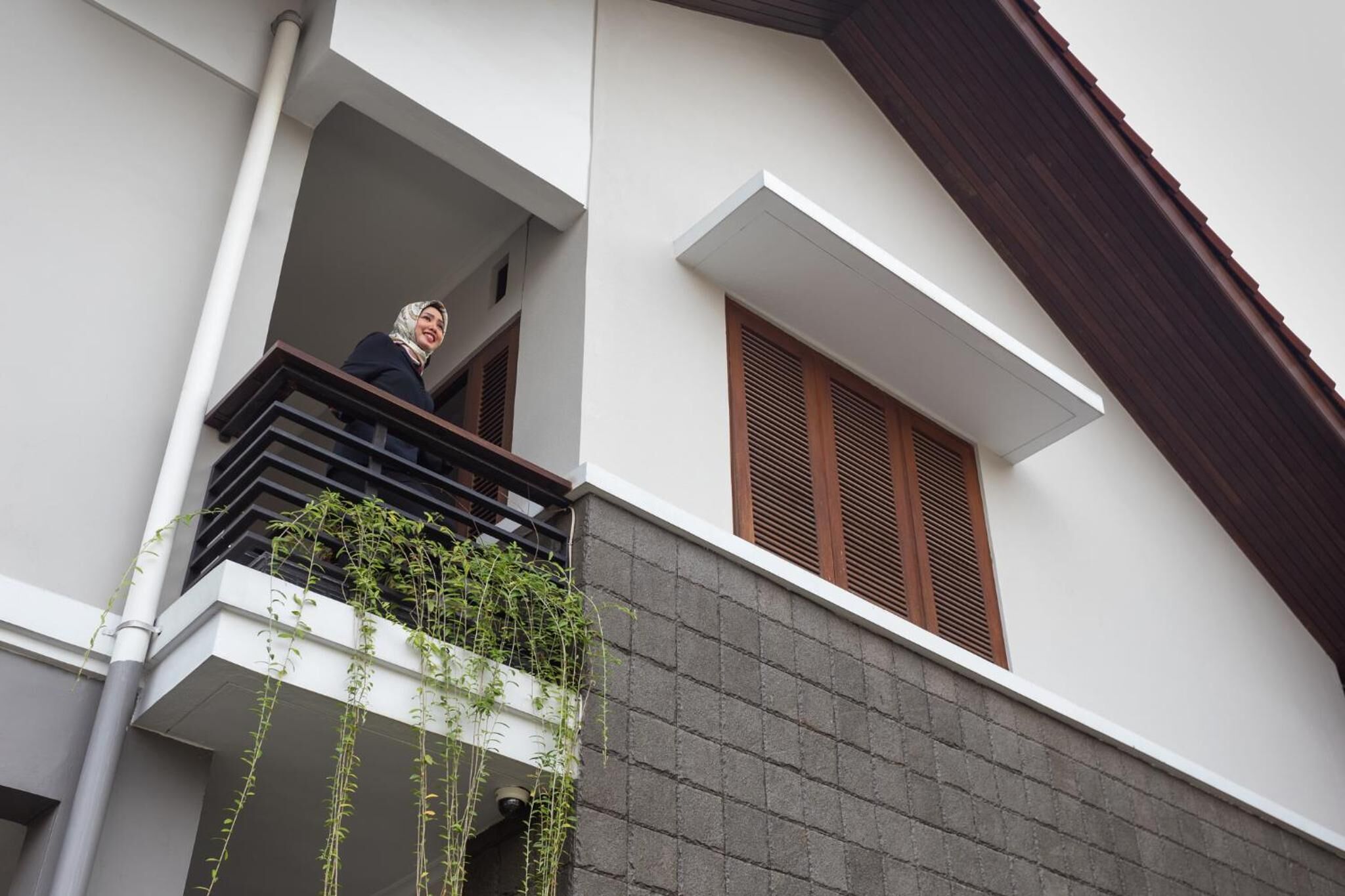 A modern building with a balcony, a window with wooden shutters, and a grey brick wall.