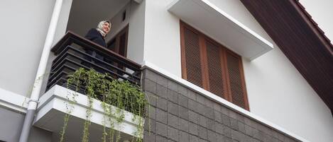 A modern building with a balcony, a window with wooden shutters, and a grey brick wall.