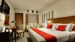 A hotel room with a large bed, a desk with a chair, a television, and a window with curtains. - Hotel Ilos (Bandung)