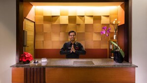 A reception desk with a wooden panel backdrop, a red flower vase, and a potted orchid. - Hotel Ilos (Bandung)