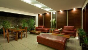 A modern living room with a wooden dining table, red leather sofas, and a stone accent wall. - Hotel Ilos (Bandung)