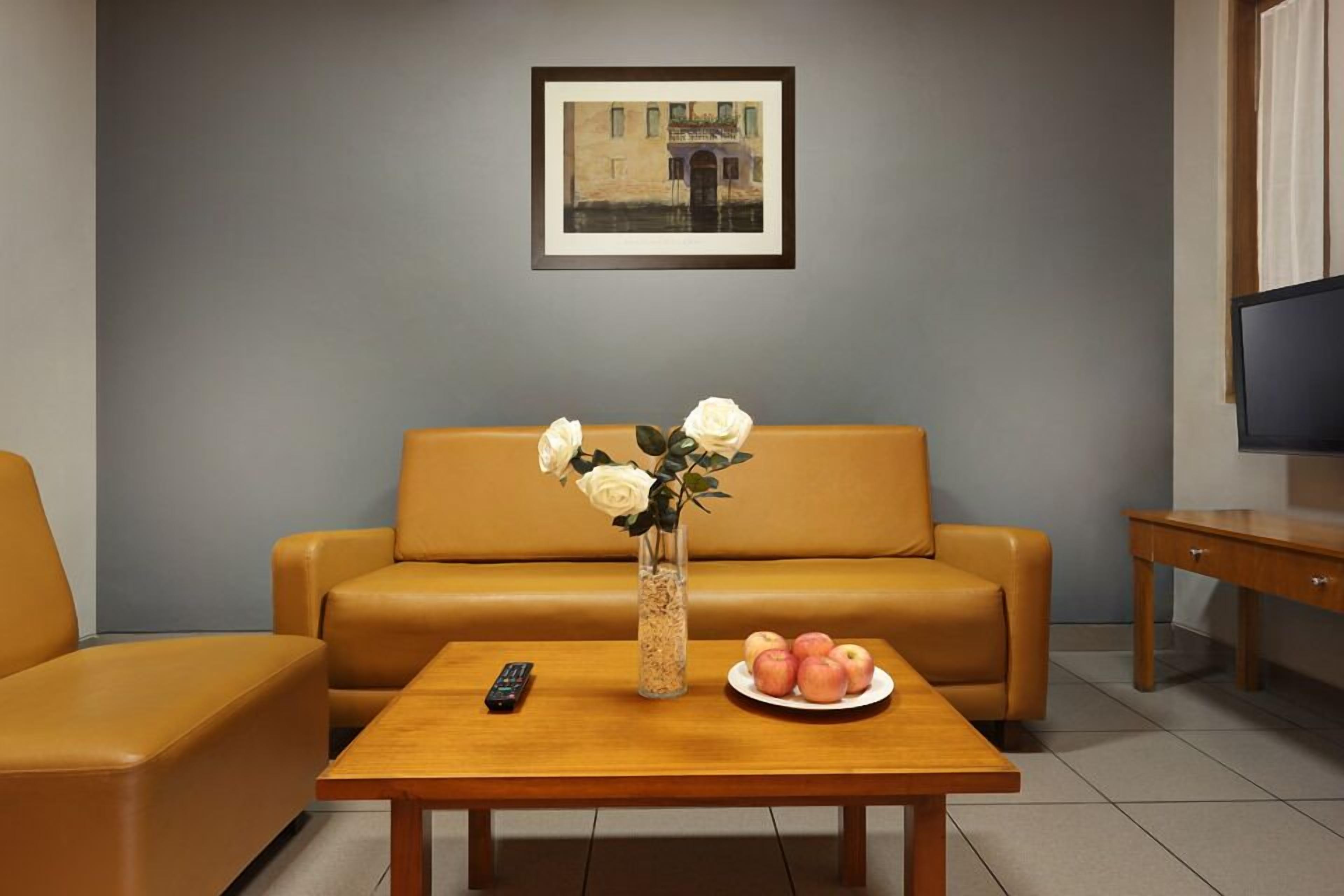 A living room with a sofa, a coffee table with a vase of flowers and a plate of apples, and a remote control on the table.