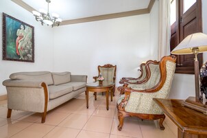 A living room with a sofa, a wooden chair, a small round table, and a lamp.