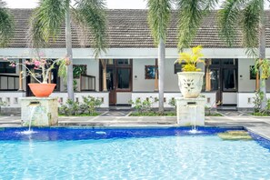 A swimming pool with a tiled deck, surrounded by potted plants and a building with a tiled roof. - Inna Bali Heritage Hotel (Denpasar)