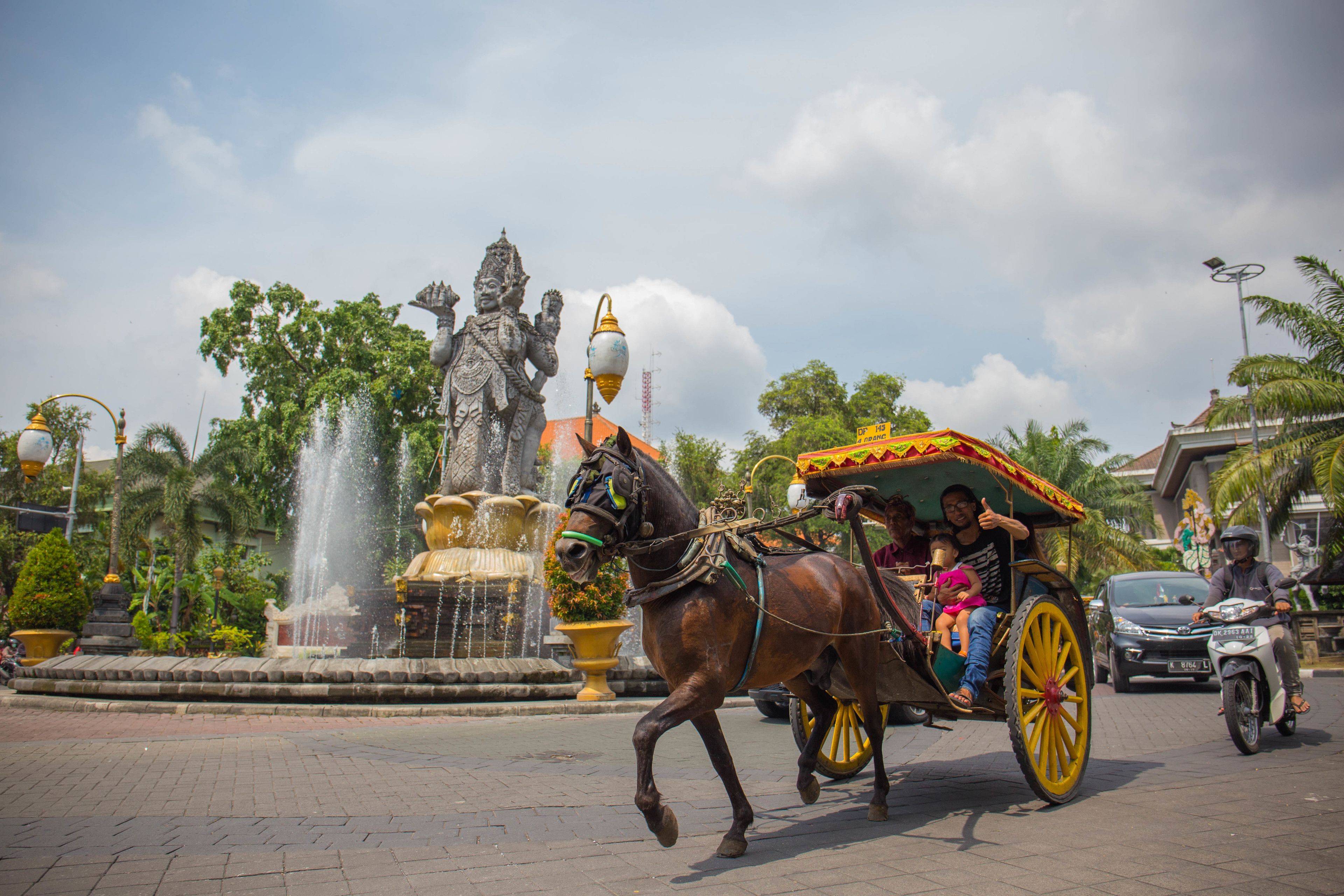 A horse-drawn carriage with passengers and a statue in the background.