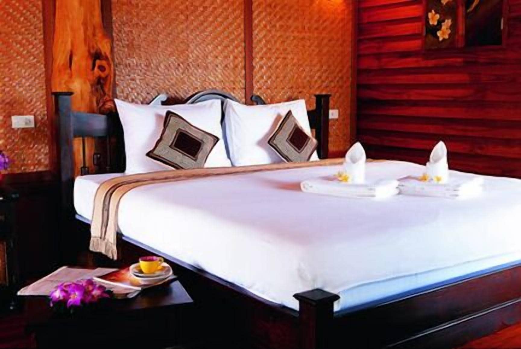 A neatly made bed with pillows, a bedside table with a cup and a menu, and a wooden wall.