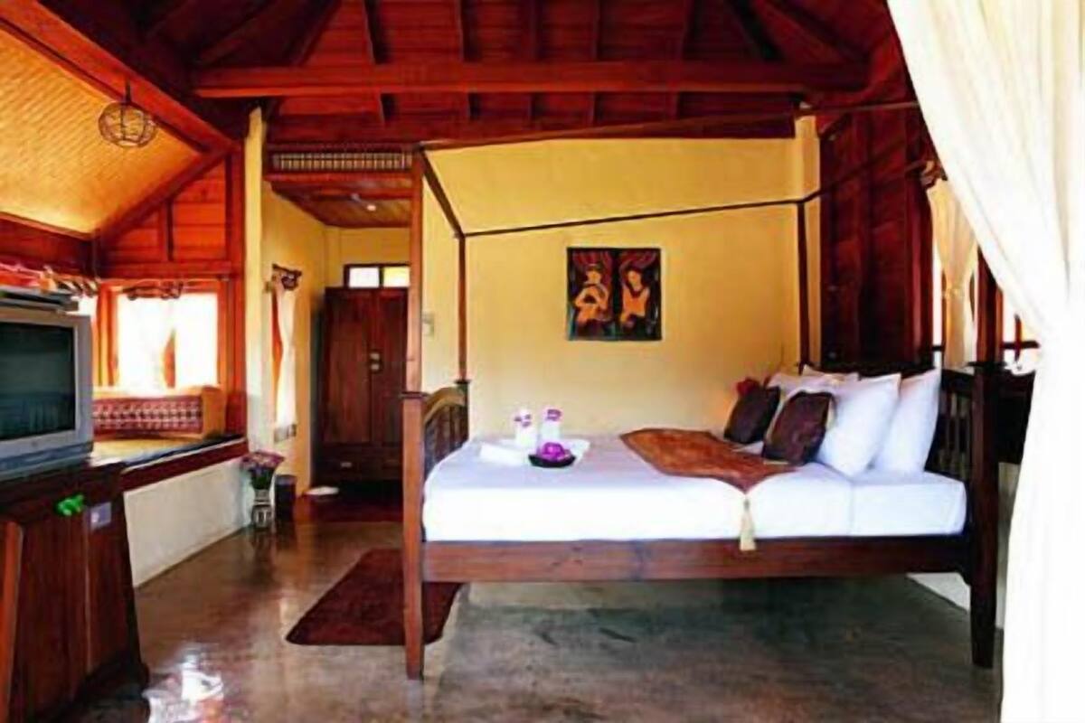 A bedroom with a bed, a television, and a painting on the wall.