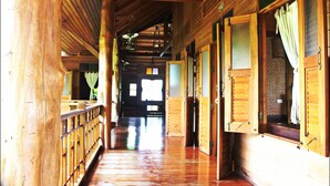 A wooden corridor with a wooden floor, wooden railings, and open doors with curtains. - Pai Vimaan Resort (Pai)