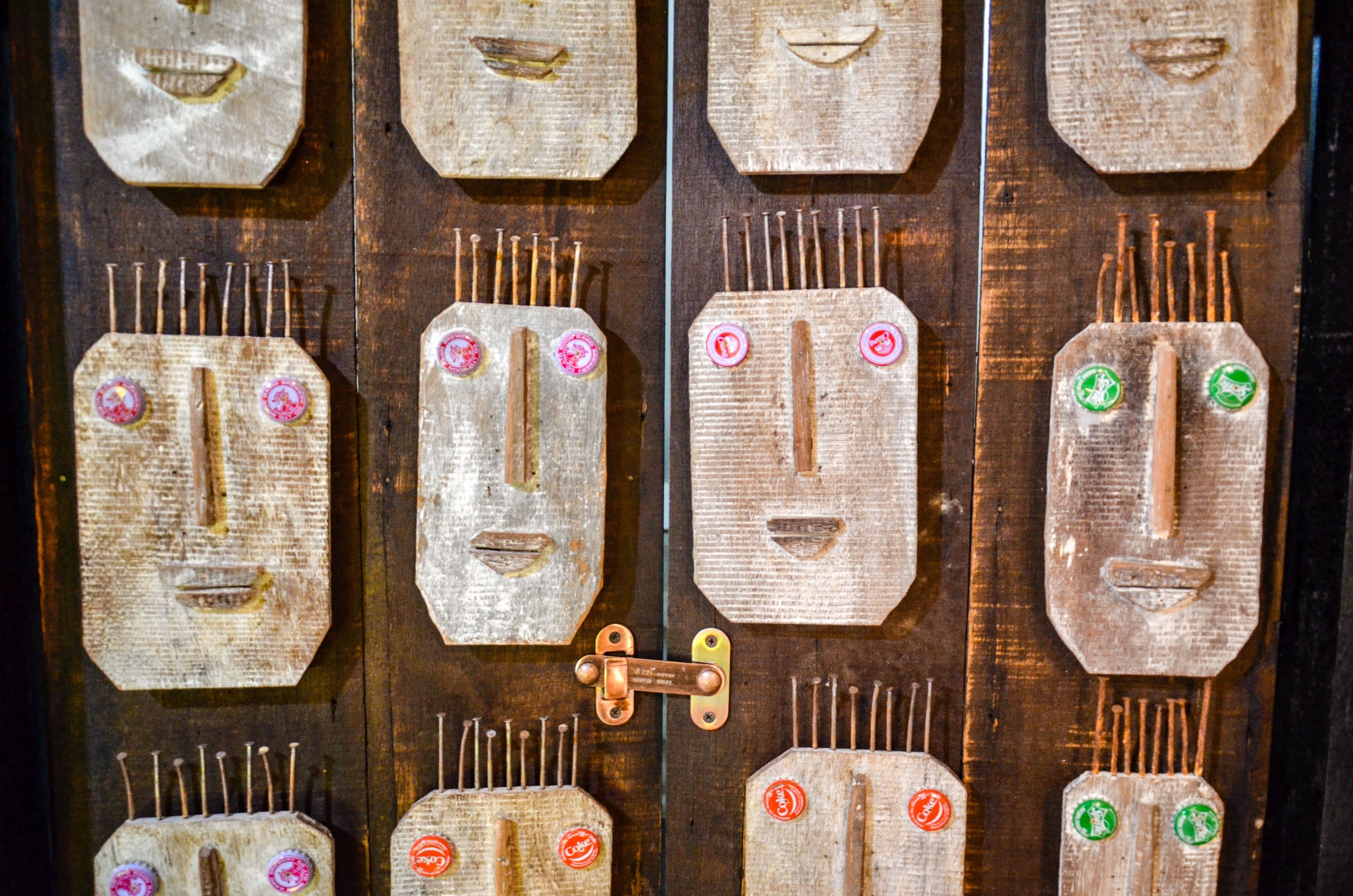 Una puerta de madera con varios paneles, cada uno con un diseño facial único y una serie de clavos.