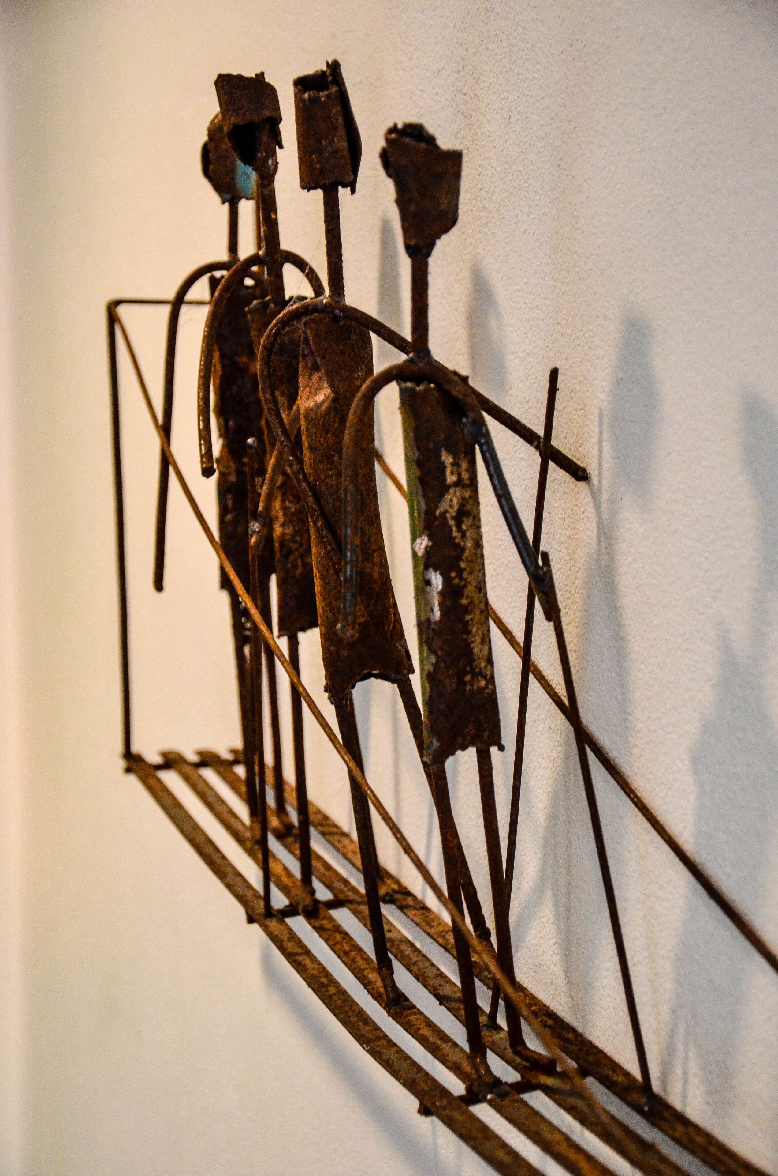 Una escultura de metal con figuras abstractas y formas geométricas fijada en una pared.