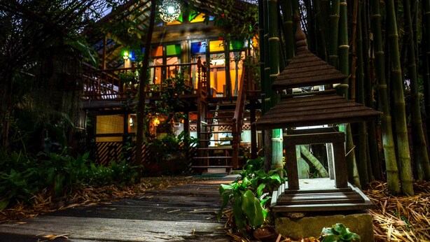 Un edificio de estilo japonés tradicional con estructura de madera y techo de paja, rodeado de bambú.