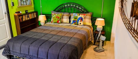 Un dormitorio con pared verde, estructura de cama metálica, colcha acolchada, dos lámparas de noche y una mesita de noche con lámpara.
