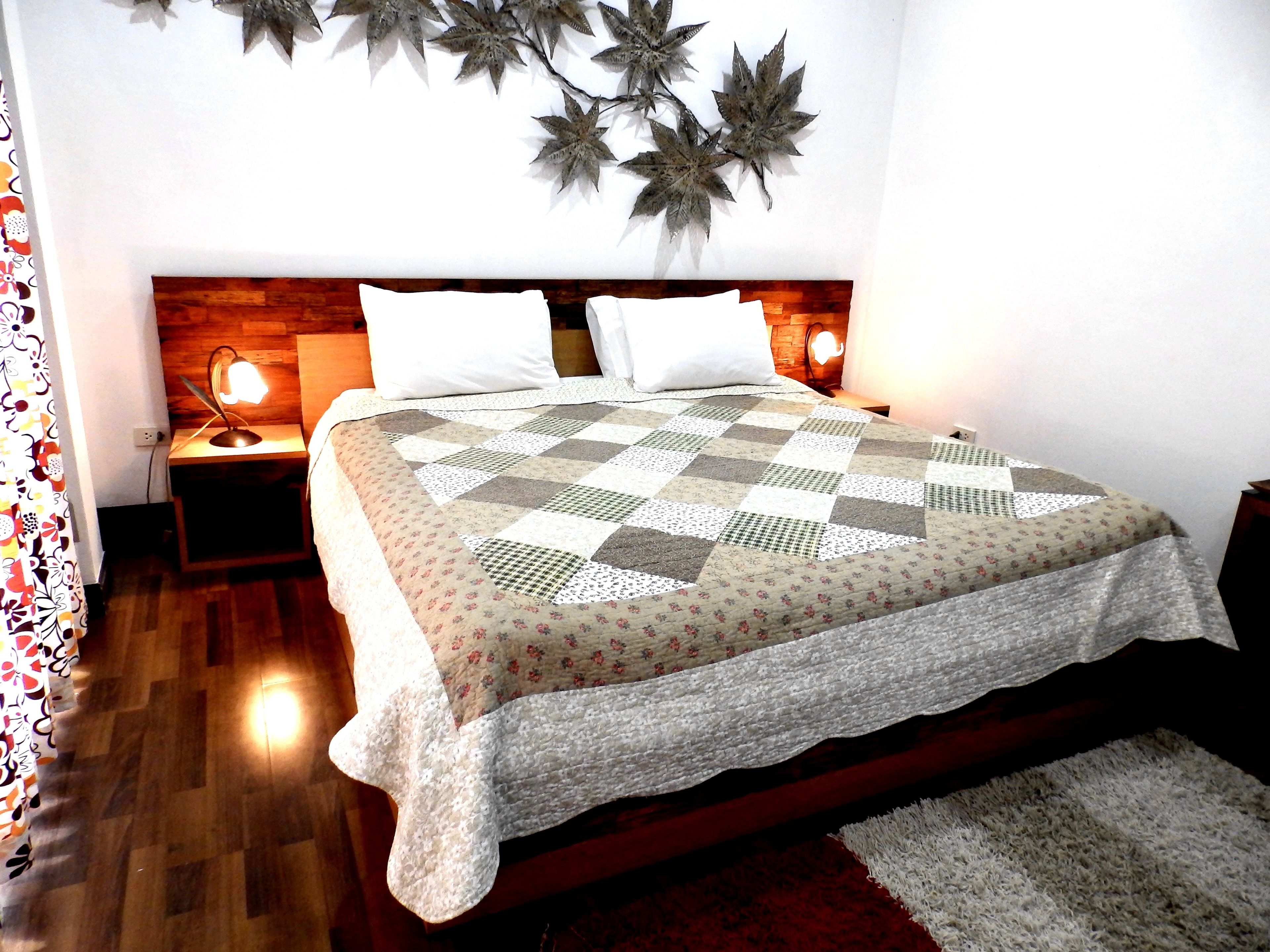 A neatly made bed with a patterned quilt, two bedside lamps, and a wall-mounted decorative leaf.