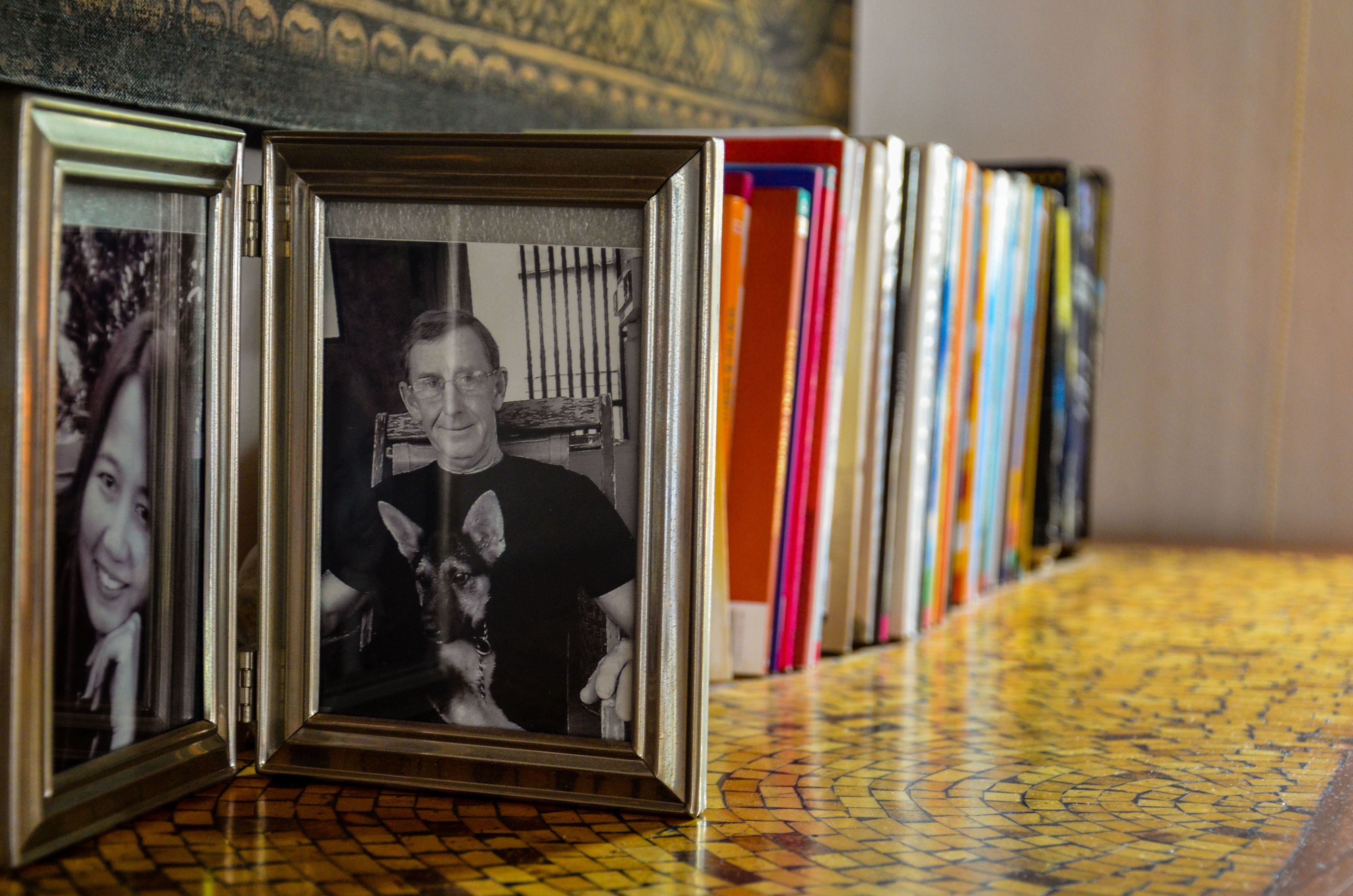 Una hilera de fotografías enmarcadas sobre un suelo de baldosas, con estanterías llenas de libros de colores al fondo.