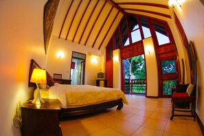 A spacious bedroom with a large bed, a nightstand with a lamp, a TV, and a view of the outdoors through a large window. - Baan salee pai (Pai)