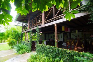 A wooden structure with a covered upper level, surrounded by lush greenery and a pathway leading to the entrance. - Baan salee pai (Pai)
