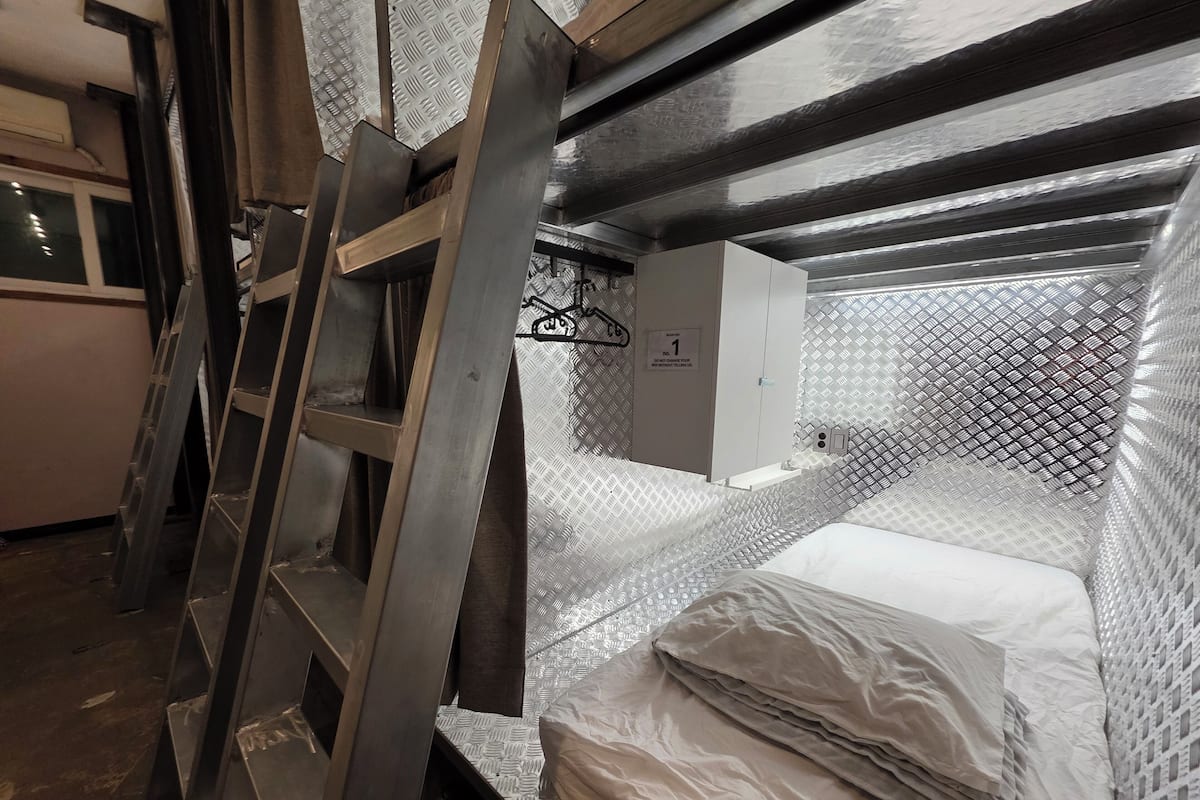 Ein Schlafraum mit Etagenbetten, Metallgitter, einem weißen Kleiderschrank und einer Wand mit Muster.