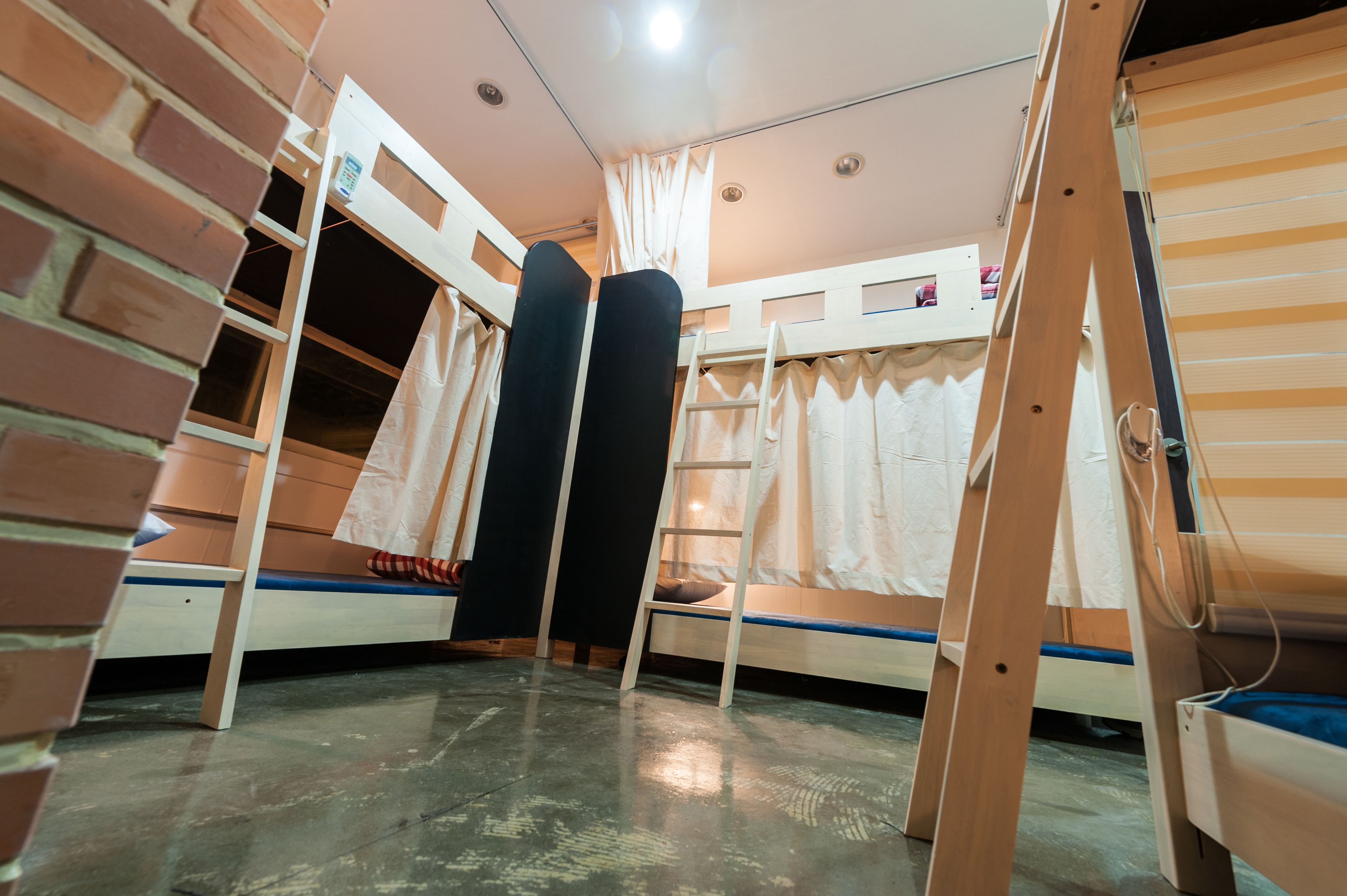 A dormitory room with bunk beds, a ladder, and a window with curtains.