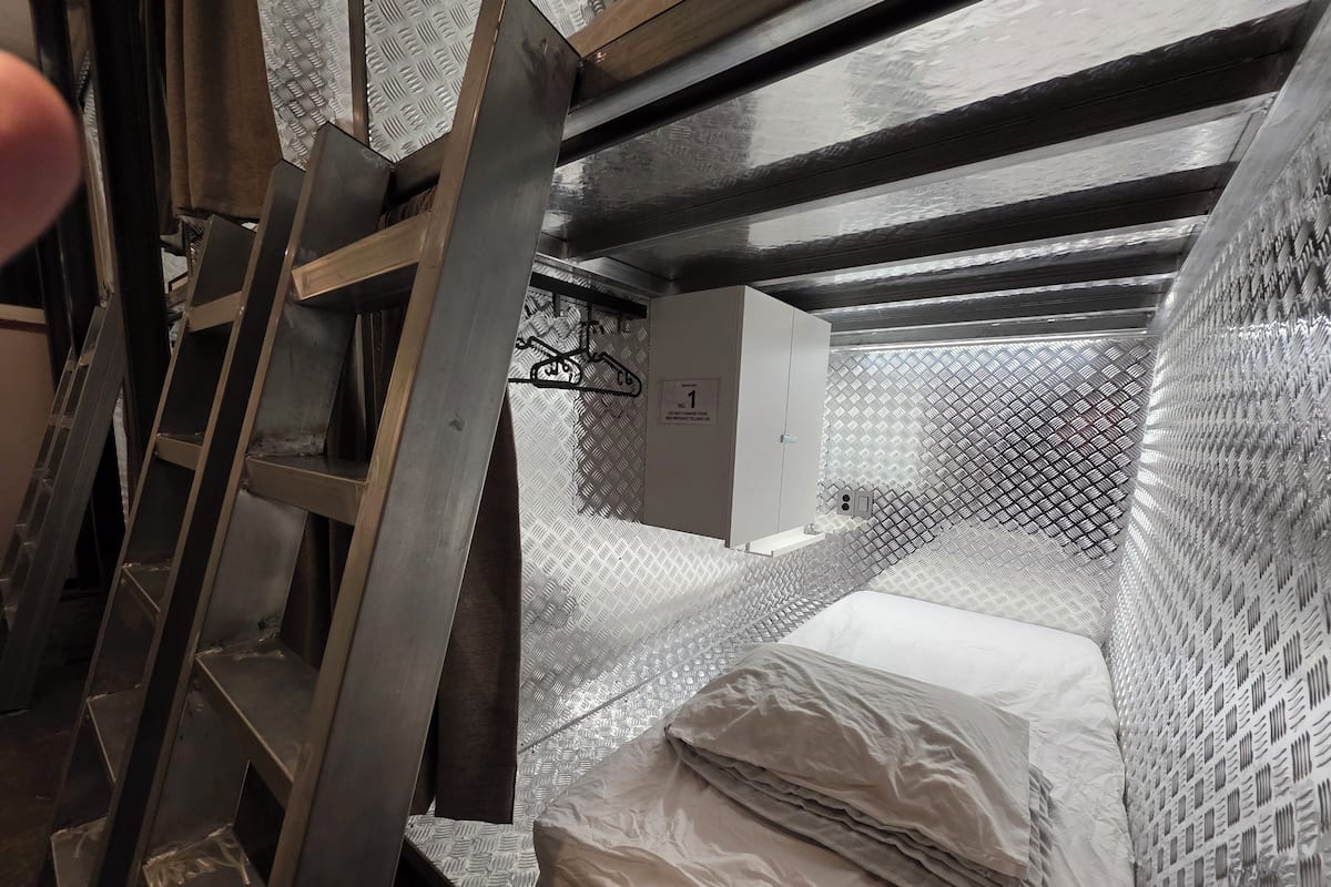 Ein Zimmer mit einer Metallleiter, einem Bett mit Metallkopfteil und einem weißen Schrank.