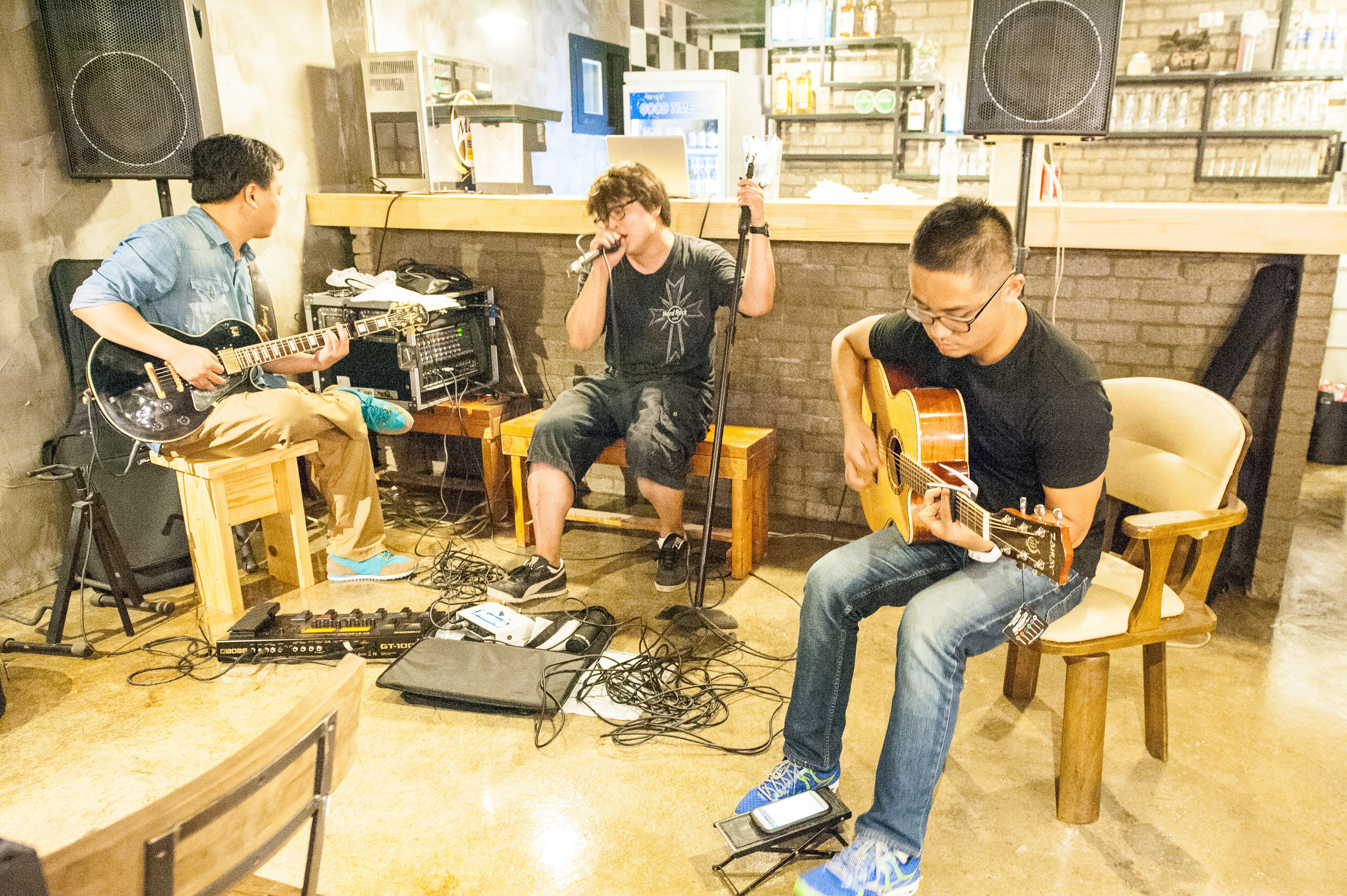 A group of musicians performing in a room with a brick wall, a bar counter, and various musical equipment.