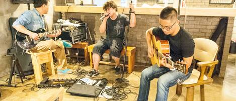 A group of musicians performing in a room with a brick wall, a bar counter, and various musical equipment.